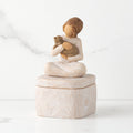 Front: cream square resin box with lid, 3-D figure of seated girl holding cat atop lid