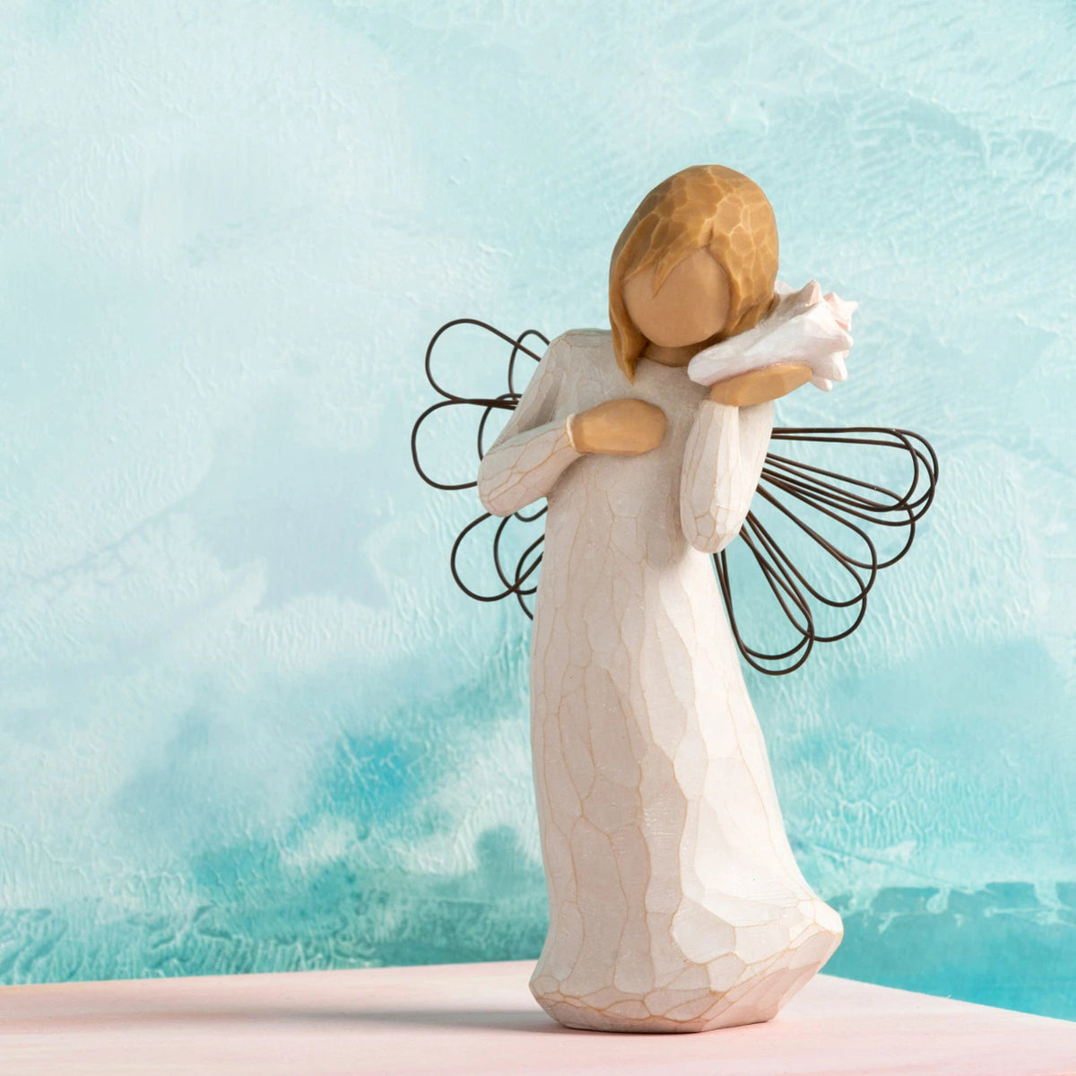 Willow Tree Thinking of You, 5.5”h hand-painted standing resin figure in cream dress with wire wings, holding pink conch shell to ear, in front of sea blue painting