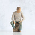 Front view, adult male figure in light gray shirt and blue jeans, seated on gray rock