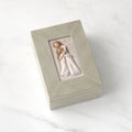 Light gray rectangular wood box with hinged lid, carving on lid of female and child embracing in cream dresses