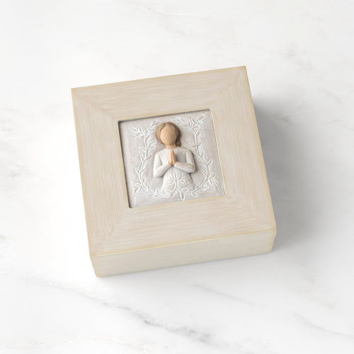 Cream square wood box with hinged lid, carving on lid of female in cream dress with hands in prayer position, surrounded by leaves and vines