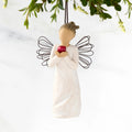 Front view of figure in cream dress with wire wings holding large red apple in hands, ornament hook on head