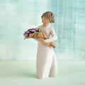 Willow Tree Surprise, 5”h hand-painted standing resin figure in cream dress, holding bouquet of purple tulips, in front of green-blue painting