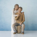 Man figurine sitting on rock wearing brown shirt and blue jeans with woman figurine in white dress with arms wrapped around him - blue background