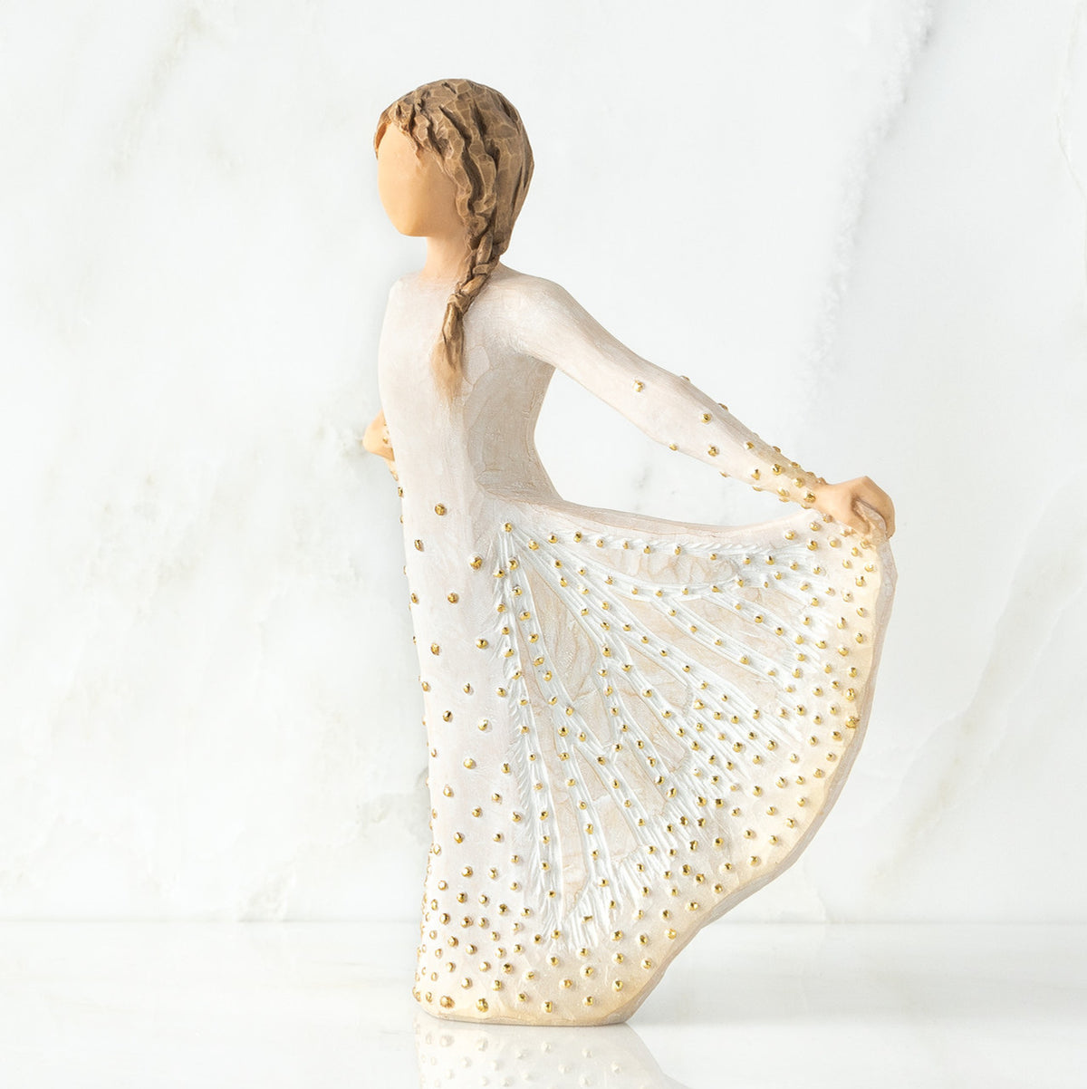 Left view of standing female figure in cream dress, holding out her skirt, which is carved with butterfly markings and dotted with gold