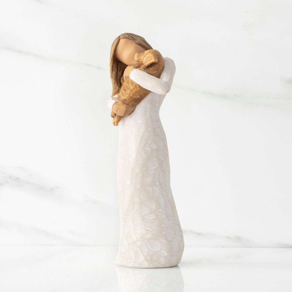 Left view, standing female figure in cream dress, holding golden color puppy in her arms