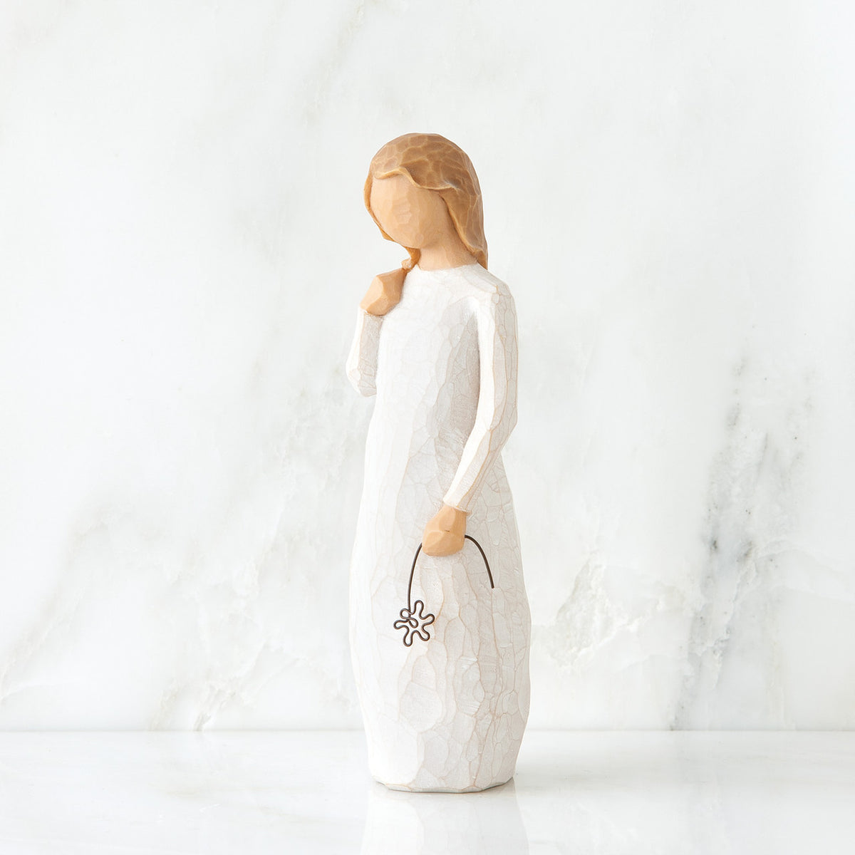 Front view of blonde girl figurine in white dress standing holding black flower