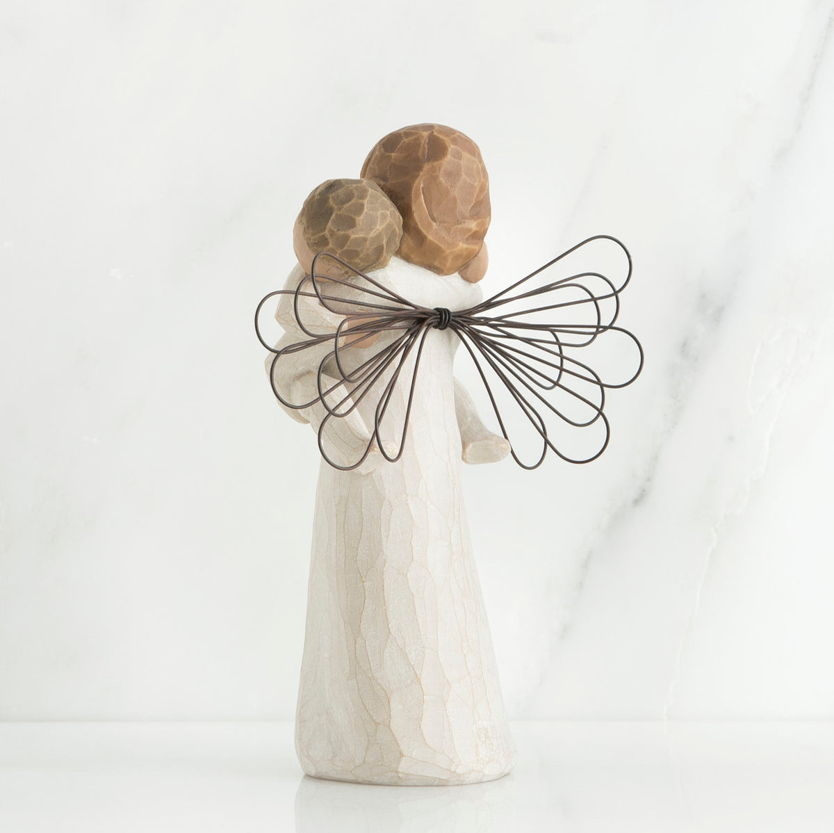 Back view of brunette girl figurine in white dress with brown wings holding baby