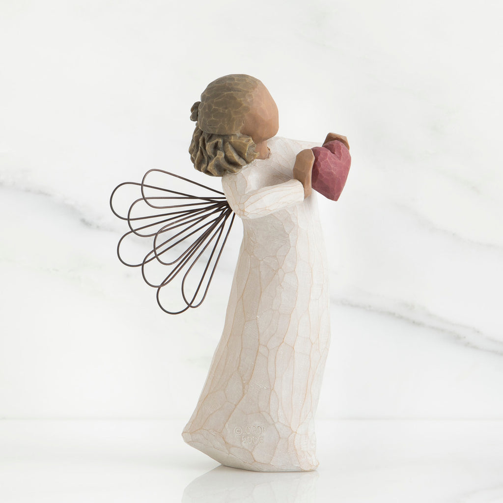 Side view of brunette angel girl figurine in white dress holding pink heart figurine