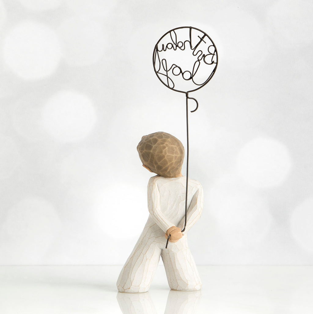 Back view of little boy with light brown hair holding a wire balloon behind his back. Text on balloon is wire