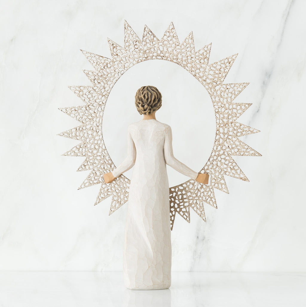 Back view of brunette girl figurine in white dress holding sun figurine up