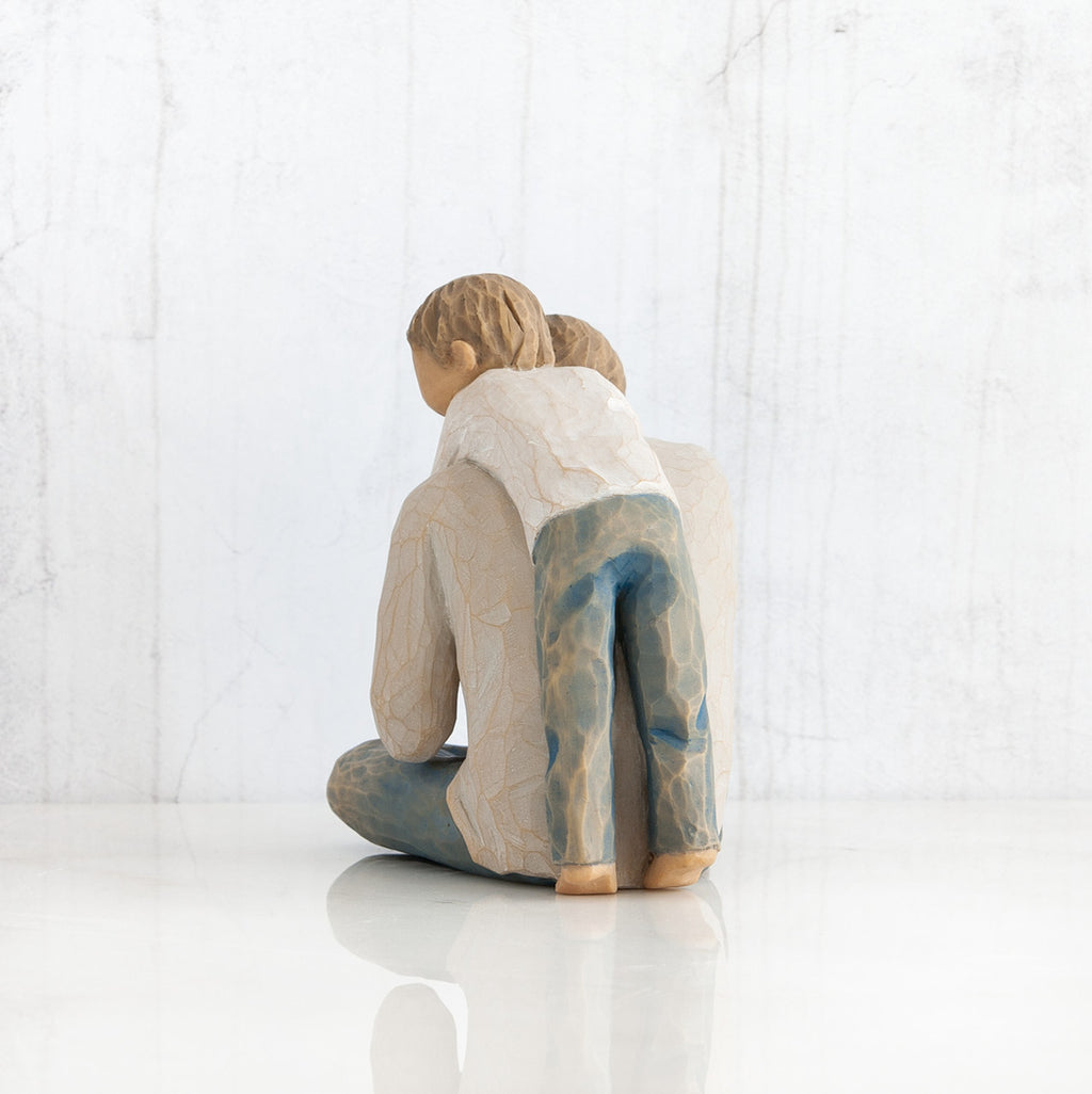 Back view of little boy figurine in blue jeans and white shirt hugging a larger father figurine