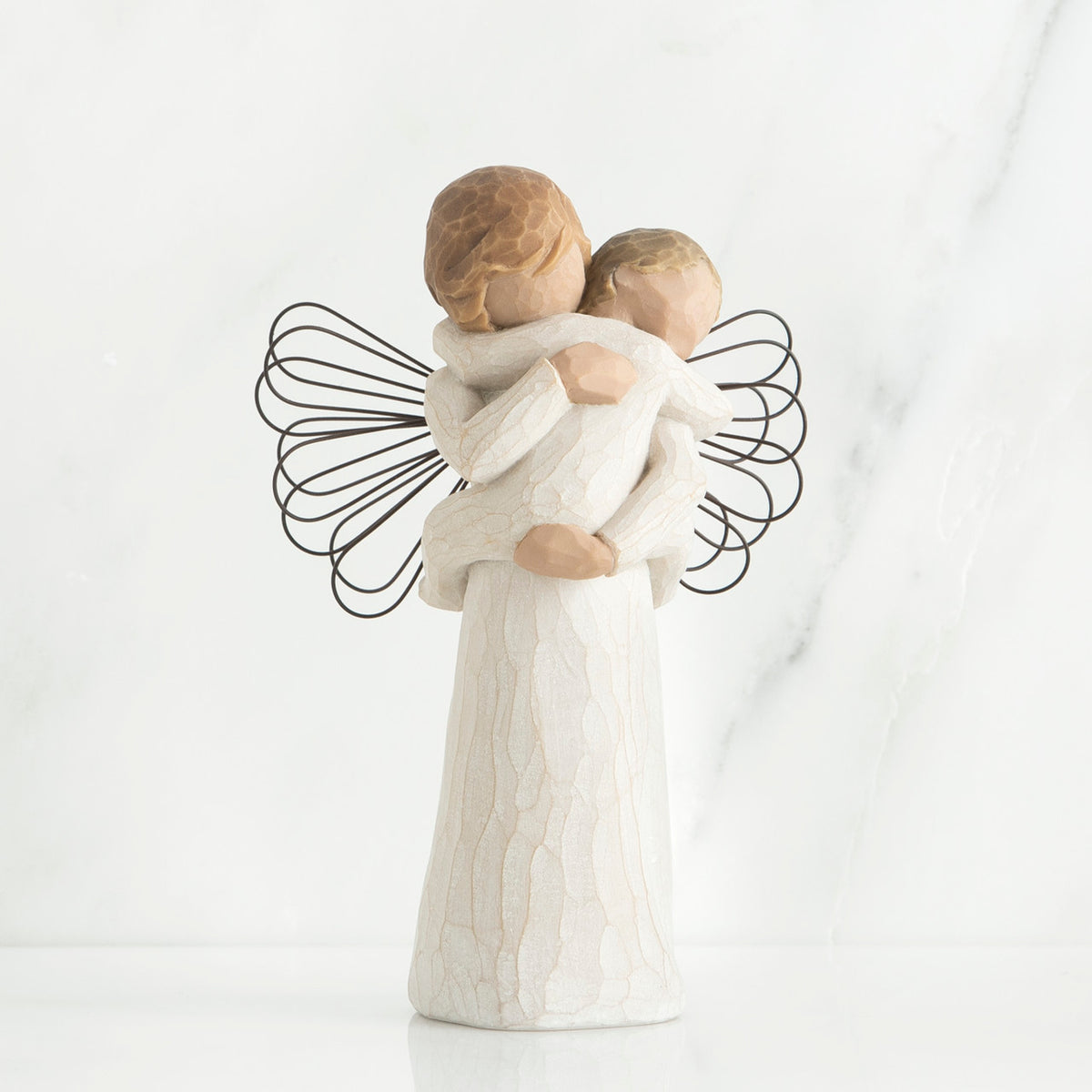 Young girl angel faceless figurine wearing white dress and has black wire wings, holding faceless baby in her arms