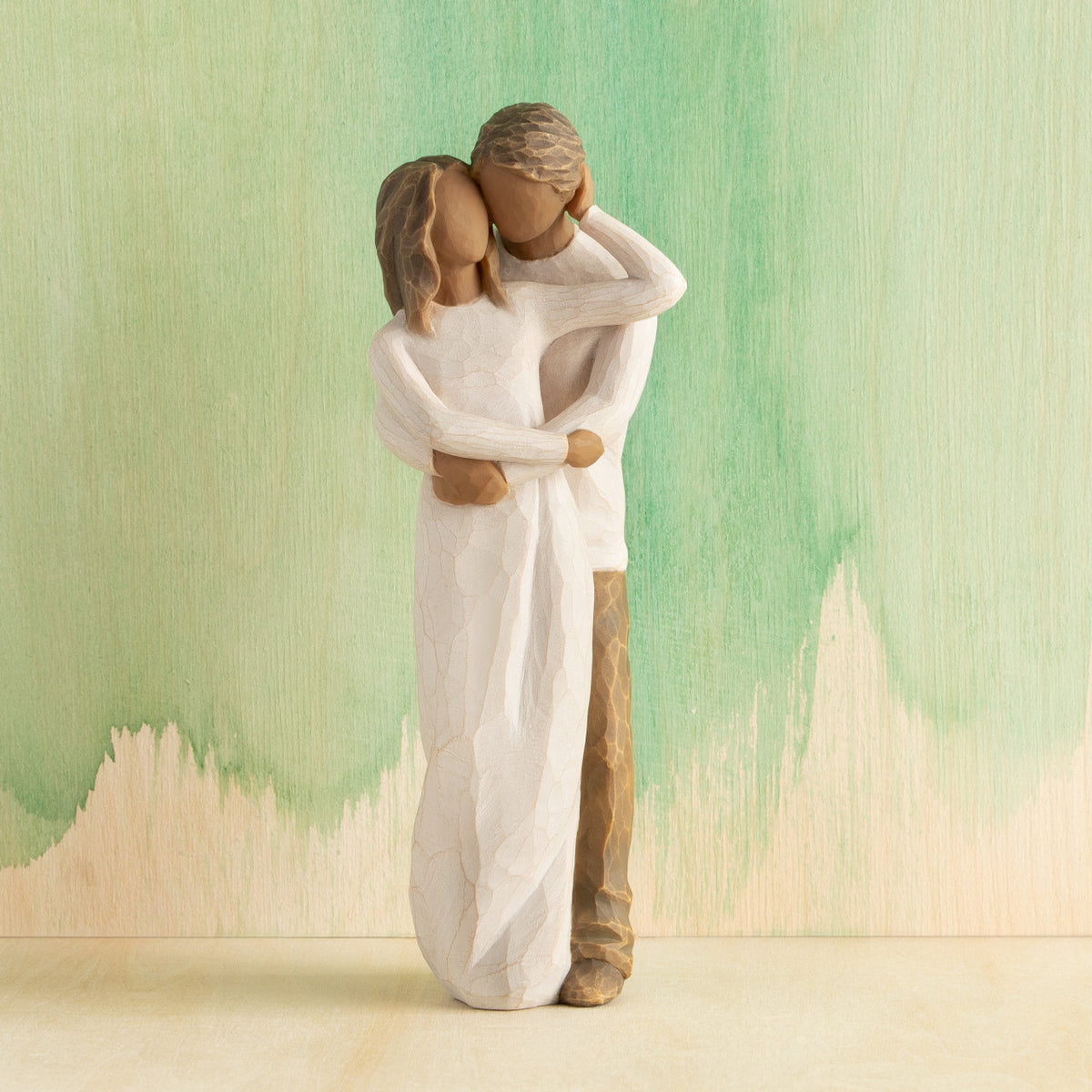 Front view of couple, standing with arms around each other. Woman and man have darker skin tones and hair color. Green painted background.
