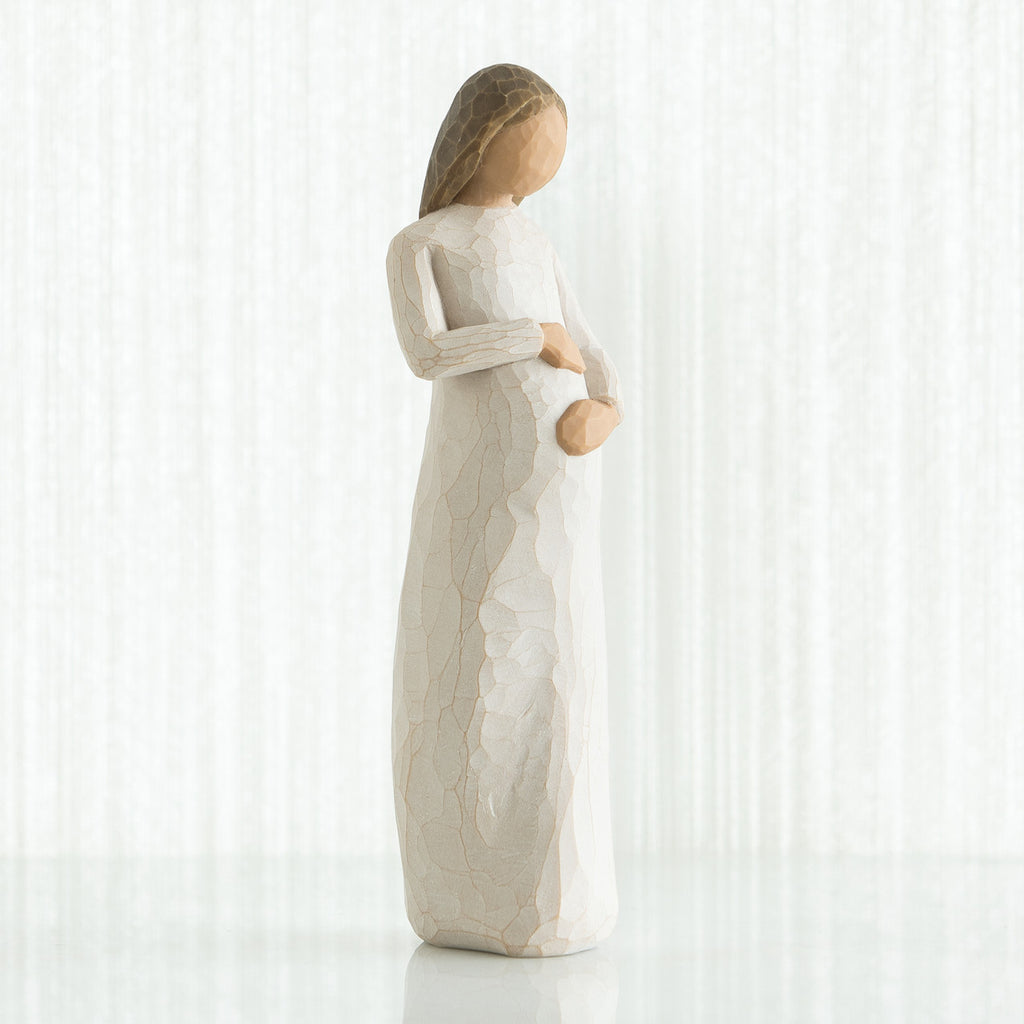 Faceless pregnant woman figurine wearing white dress with hands clutching her stomach
