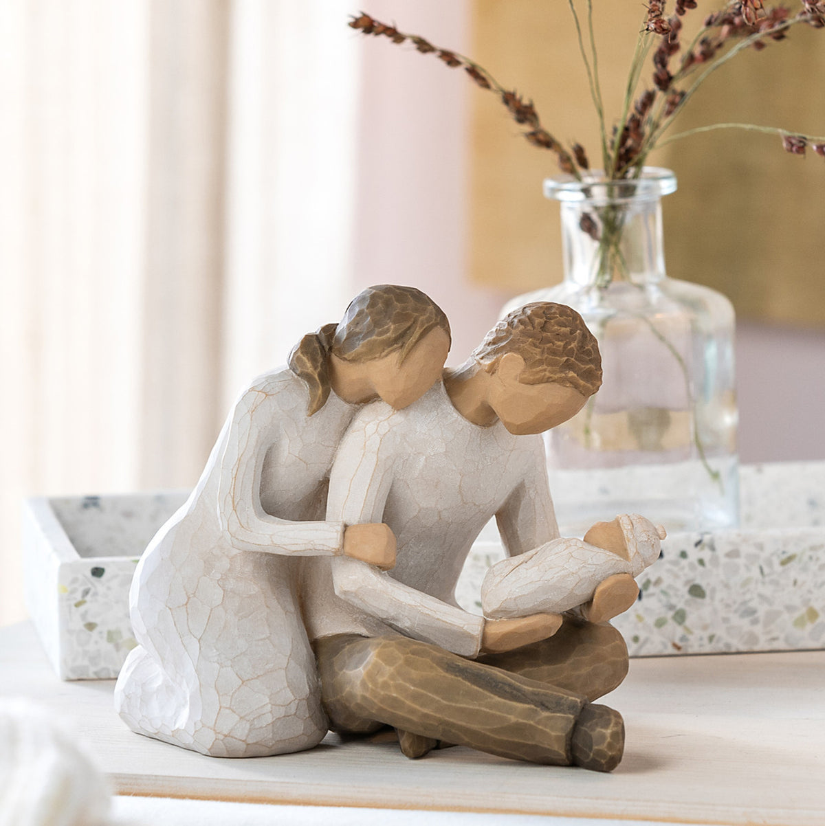 Willow Tree New Life, 5”h hand-painted resin figure of seated couple in neutral colors, holding newborn baby wrapped in cream blanket, on bedroom dresser