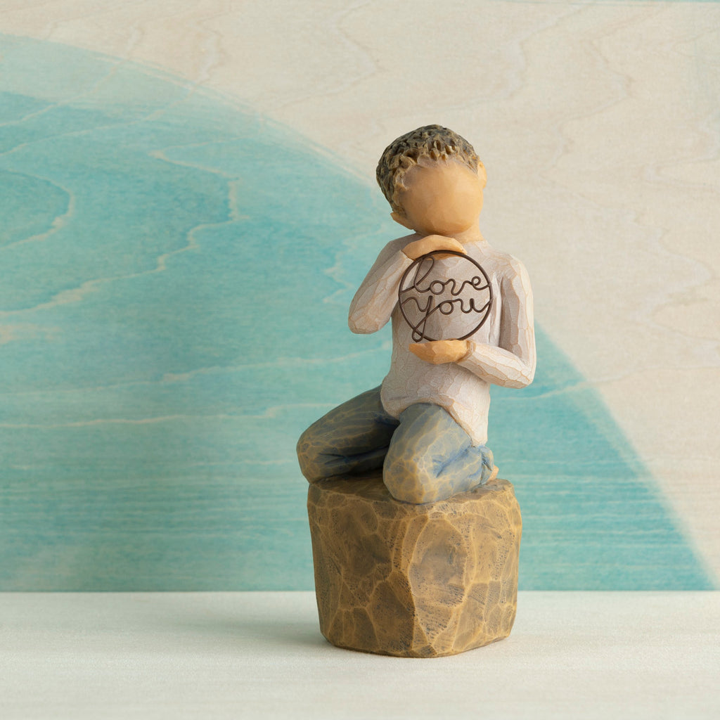 Willow Tree Love you too (lighter skin), 4.5”h hand-painted resin figure of young child in cream shirt and jeans, kneeling on rock, holding wire circle with ‘love you’ inside, in front of blue painting