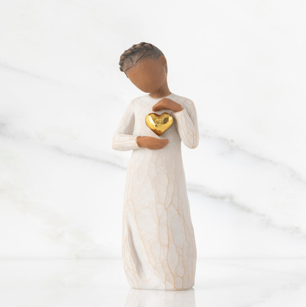 Front view: standing figure in cream dress with darker skin and dark hair braid, framing gold leaf heart with both hands on chest