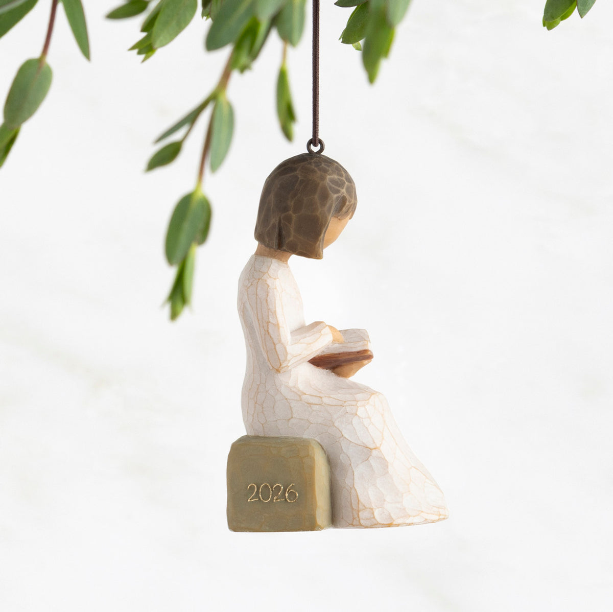 Profile view: Ornament of seated figure reading a book; 2026 in raised gold numbers on rock; loop and hook in head